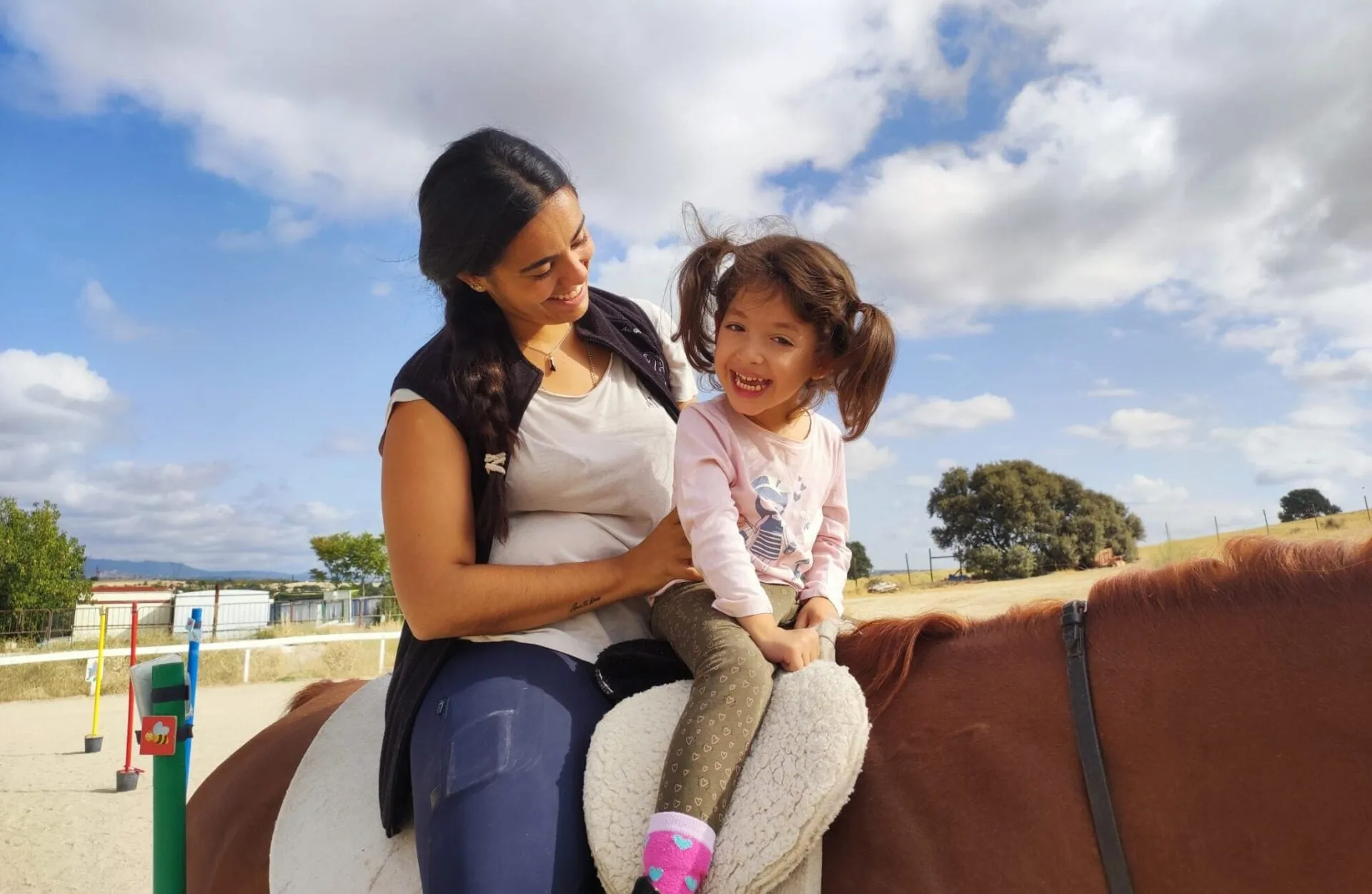 Una terapeuta sujeta a una niña pequeña sentada sobre el caballo durante una sesión