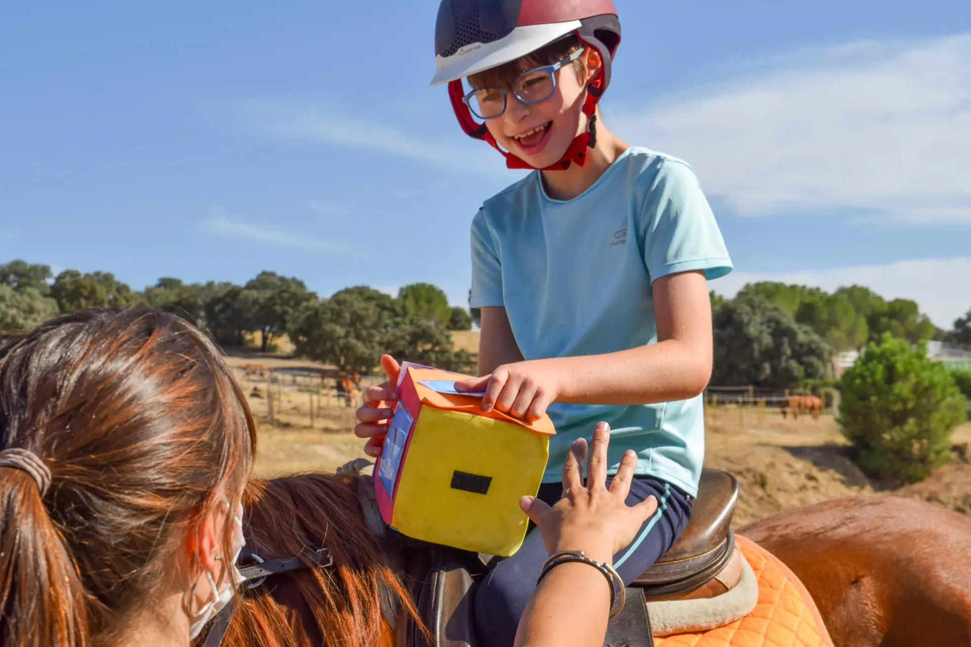 Sesión de hipoterapia: una niña sonríe a caballo mientras trabaja con material didáctico junto a su terapeuta