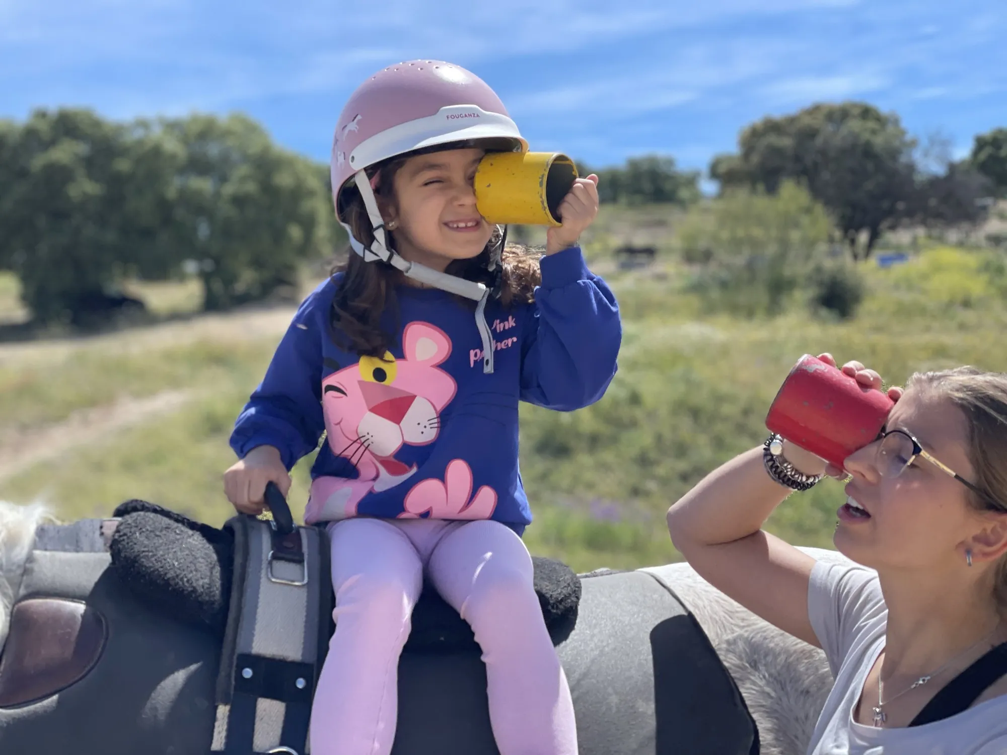 Una niña a caballo mira por un vaso de colores imitando a su terapeuta durante la sesión