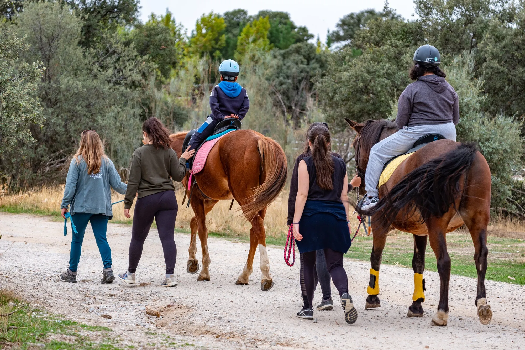 Monitoras acompañan a dos jinetes en un paseo a caballo por el campo