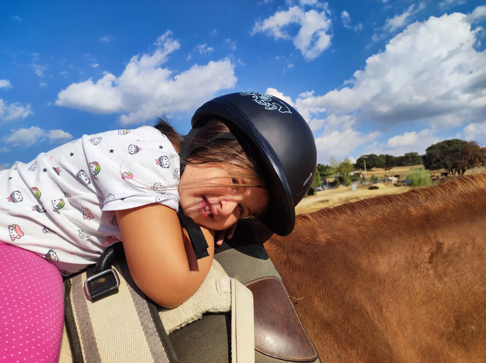 Una niña con casco sonríe abrazada al cuello del caballo