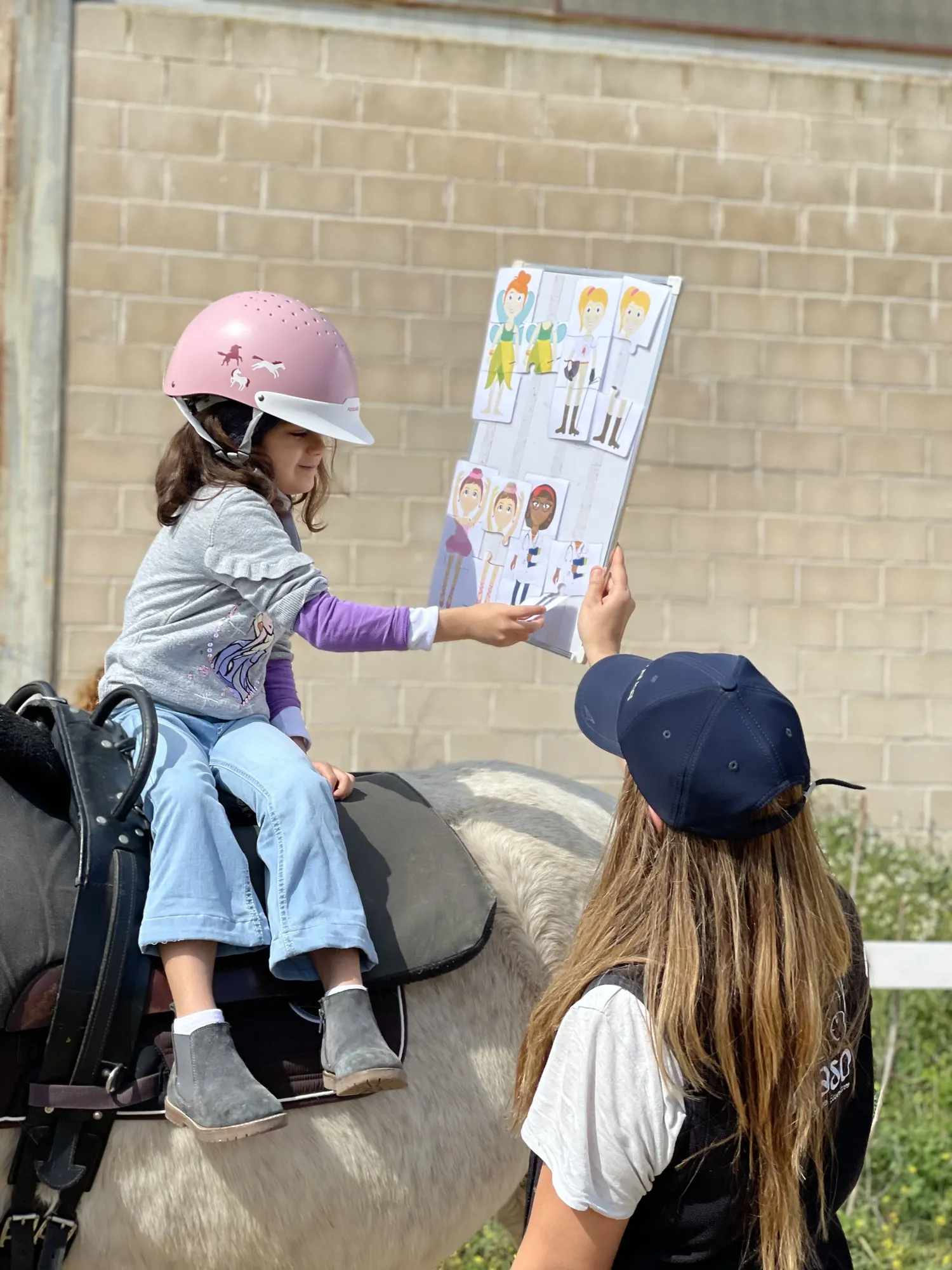 Una niña a caballo trabaja con un panel de pictogramas que le enseña la terapeuta